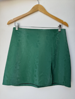 Pollera corta verde con estampado de serpiente, colgada en un perchero de madera.