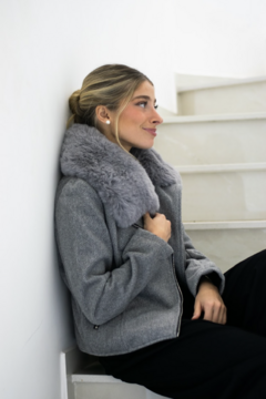 Mujer sentada en una escalera, usando una campera gris con un cuello de piel sintética gris claro.