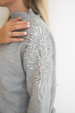 Sweater largo con diseño de strass en los hombros que caen por la manga. Cuello alto. Color gris