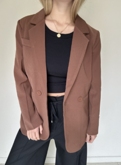 Modelo vistiendo un blazer marrón con botones, combinado con una camiseta negra y pantalones oscuros.