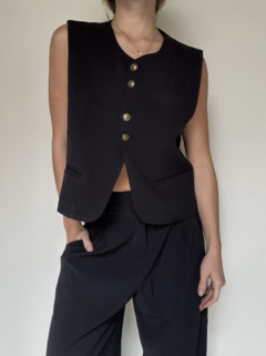 Chaleco Sastrero negrocorto, con botones dorados﻿ y bolsillos delanteros. En combinación con pantalón ancho estilo sastrero, con botón y cierre.