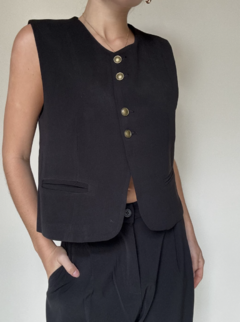 Chaleco Sastrero negrocorto, con botones dorados﻿ y bolsillos delanteros. En combinación con pantalón ancho estilo sastrero, con botón y cierre.