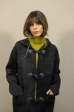 Tapado Almendra negro de mujer con capucha y cierres de broche, combinado con suéter de cuello alto verde.