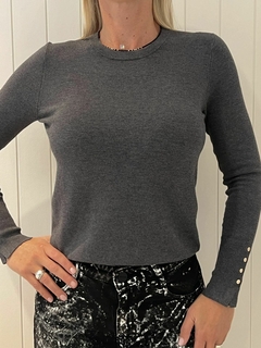 Modelo usando un suéter gris de Zara con botones en las mangas, combinado con pantalones oscuros.
