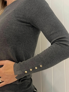 Suéter gris de Zara con detalles de botones dorados en la manga.