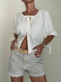 Modelo vistiendo shorts cortos de color claro con una blusa blanca y cinturón.