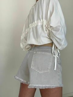 Modelo usando shorts cortos de denim en color claro, con un top blanco y detalles de cintas en la espalda.