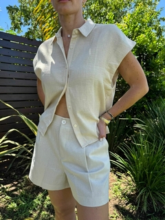 Mujer posando con una camisa beige y shorts cortos de tela ligera en un entorno natural.