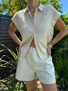 Mujer luciendo un conjunto de camisa y shorts de color claro, con un fondo de plantas verdes.