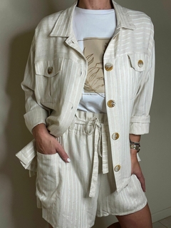 Un conjunto de ropa que incluye una camisa de botones color crema y un short a juego, con un diseño de rayas sutiles.