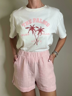 Remera blanca con estampado de palmeras y texto "THE PALMS SURF CLUB 1985", combinada con pantalones cortos rosa.