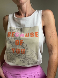 Remera Beca sin mangas con un diseño gráfico que dice "BECAUSE OF YOU" sobre un fondo de mapa.