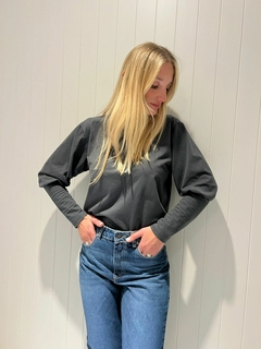 Mujer posando con una remera negra de manga larga y jeans, frente a una pared blanca.