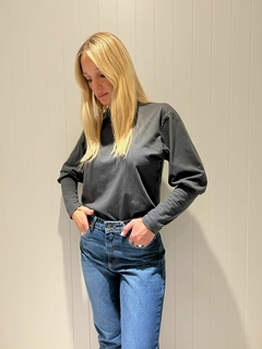 Modelo luciendo una remera negra de manga larga, combinada con jeans de tiro alto frente a una pared blanca.
