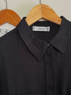 Primer plano de una camisa negra con botones y cuello, colgada en un perchero de madera.