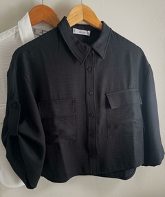 Camisa negra de manga larga con dos bolsillos frontales, colgada junto a una camisa blanca.