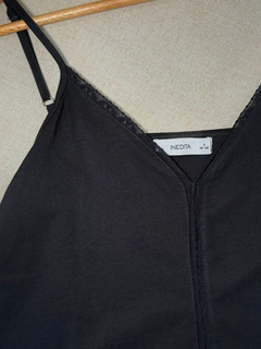 Detalle de una remera negra sin mangas con encaje en el escote y etiqueta de la marca INEDITA.