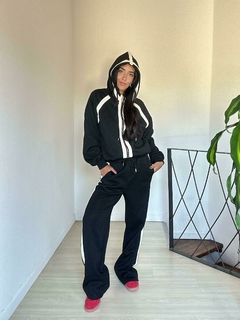 Mujer usando un conjunto de chándal negro con detalles en blanco, posando en un ambiente moderno.