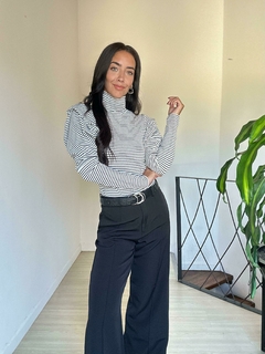 Modelo posando con una polera a rayas negras y blancas, combinada con pantalones oscuros y un cinturón negro.
