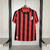 Camisa do Milan Edição Especial 125 anos, com listras vermelhas e pretas, pendurada em um cabide. Fut Outlet