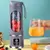 Espremedor portátil USB com frutas vermelhas e azuis, copo de suco ao lado.