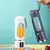 Espremedor portátil USB, com uma jarra branca contendo suco laranja e outra jarra cinza com água.