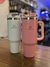 Vasos térmicos Stanley The Adventure Quencher Tumbler en colores blanco y rosa, con tapa y asa, sobre una mesa de madera.