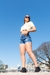Mujer posando con shorts de mezclilla y camiseta amarilla en un día soleado, con fondo de ciudad.