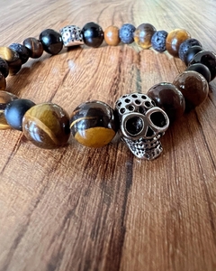 Pulsera con calavera de metal acompañada de piedras naturales de ojo de tigre y obsidiana , enhebradas sobre tanza elástica. En diferentes medidas de talle.