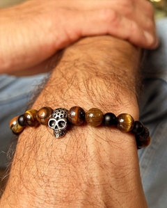 Pulsera con calavera de metal acompañada de piedras naturales de ojo de tigre y obsidiana , enhebradas sobre tanza elástica. En diferentes medidas de talle.
