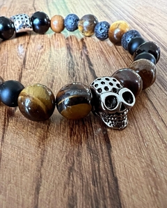 Pulsera con calavera de metal acompañada de piedras naturales de ojo de tigre y obsidiana , enhebradas sobre tanza elástica. En diferentes medidas de talle.