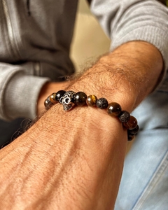 Pulsera con calavera de metal acompañada de piedras naturales de ojo de tigre y obsidiana , enhebradas sobre tanza elástica. En diferentes medidas de talle.