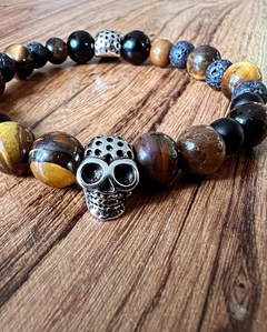 Pulsera con calavera de metal acompañada de piedras naturales de ojo de tigre y obsidiana , enhebradas sobre tanza elástica. En diferentes medidas de talle.