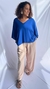 Mulher sorridente vestindo blusa goiaba azul royal de manga curta com decote em V, calça bege ampla e sandália animal print, em fundo branco