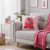 Almofada quadrada rosa com estampa do personagem Lotso Baby Fruit do filme Toy Story, apoiada em um sofá cinza claro com uma manta rosa ao lado