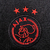 Logotipo bordado do Ajax com três estrelas vermelhas, em fundo preto.