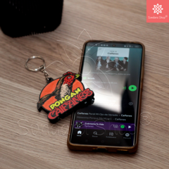Llavero "Pongan Caifanes" con diseño colorido, junto a un teléfono mostrando la playlist de Caifanes en la aplicación de Spotify.
