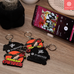 Llavero "Pongan Caifanes" con chip NFC, mostrando varios llaveros coloridos sobre una mesa junto a un teléfono que reproduce música de Caifanes.