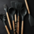 Conjunto de utensílios de cozinha em silicone preto com cabos de madeira, incluindo espátulas, conchas e pincel.