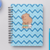 Caderno A5 com capa azul em padrão zig-zag, apresentando uma capivara sentada sobre livros.