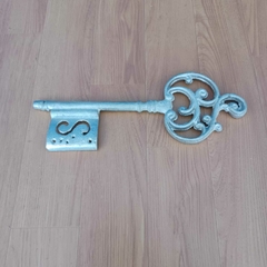 Chave decorativa em metal com acabamento prateado e arabescos detalhados.