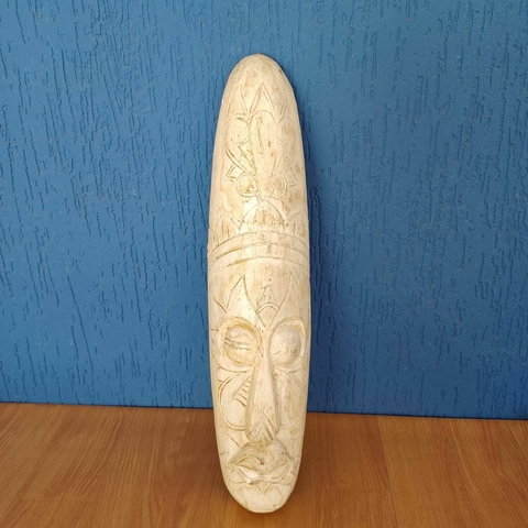 Máscara decorativa esculpida em madeira clara com entalhes tribais