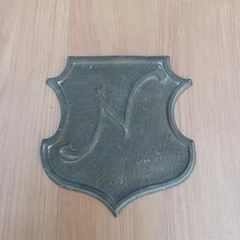 Peça decorativa em bronze com formato de escudo clássico e a letra “N”