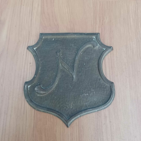 Peça decorativa em bronze com formato de escudo clássico e a letra “N”