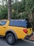 Capota Torden Adventure em uma Mitsubishi Triton amarela, destacando seu design e funcionalidade junto ao Rack de teto da capota, com vegetação ao fundo.