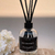 Frasco de Difusor de Aromas Chá Branco com bastões pretos, decorado com flores brancas ao lado.