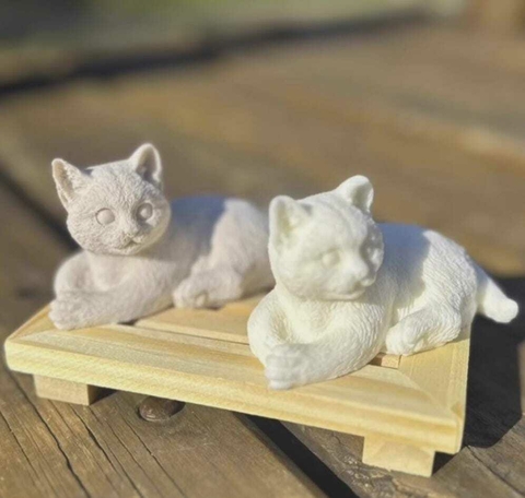 Sabonete artesanal em forma de gatos brancos, apoiado em uma base de madeira clara.