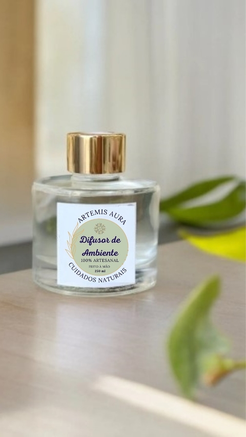 Aromatizador de ambiente em frasco de vidro com tampa dourada, da marca Artemis Aura, sobre uma mesa de madeira.