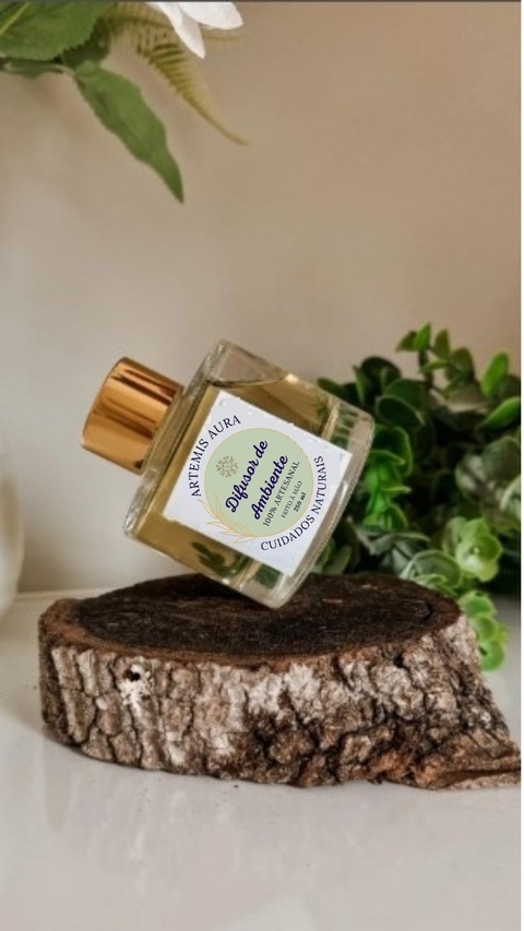 Frasco de vidro de 200ml do aromatizador de ambiente Artemis Aura, delicadamente posicionado sobre um tronco de madeira, com verdejantes ao fundo.