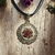 Colar com flores tons de rosa bordadas na medalha dourada com borda e fios pretos - comprar online